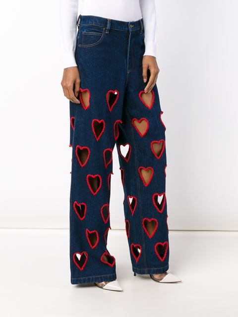 Flared jeans with heart-shaped holes along the leg, highlighted with red thread
